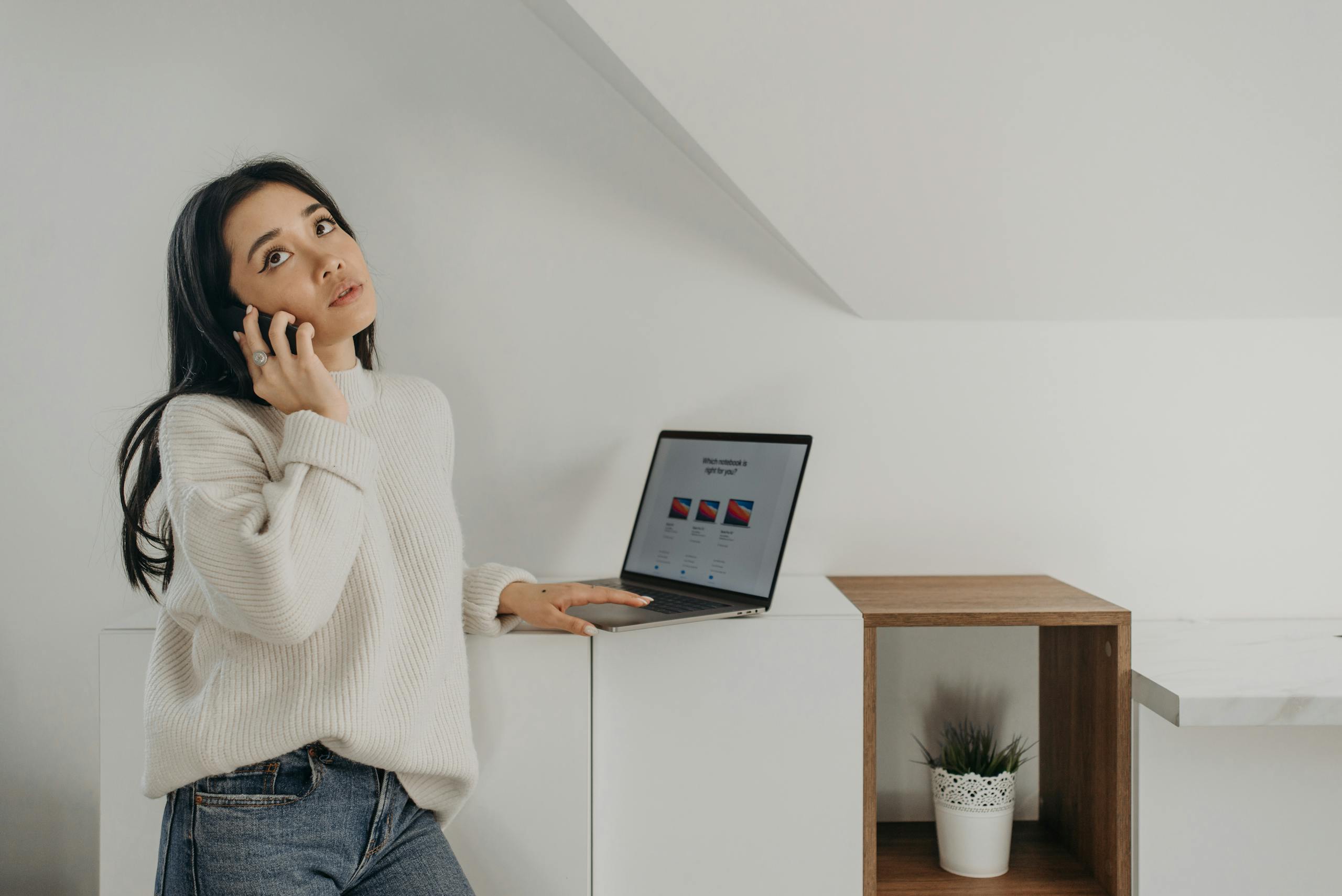 Young woman multitasking with a phone call and a laptop in a modern indoor setting.